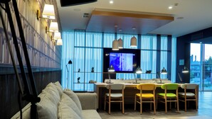 A modern living room with a sofa, dining table, chairs, and a TV. - Flag Hotel Caldas da Rainha (Caldas da Rainha)