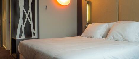 Una habitación de hotel con una cama grande, una lámpara fijada a la pared y un panel decorativo.