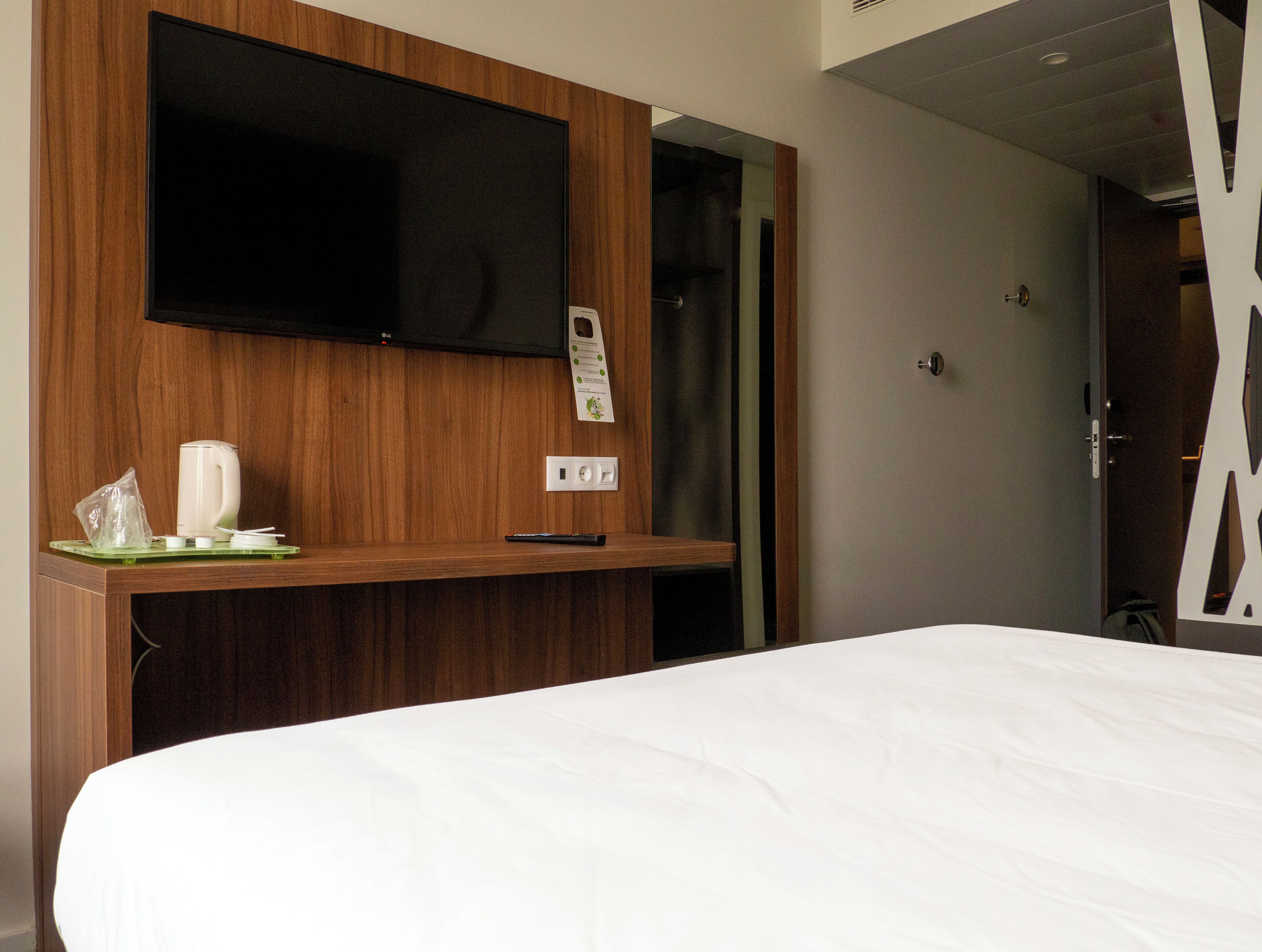 A hotel room with a bed, a mounted TV, a coffee maker, and a power outlet.