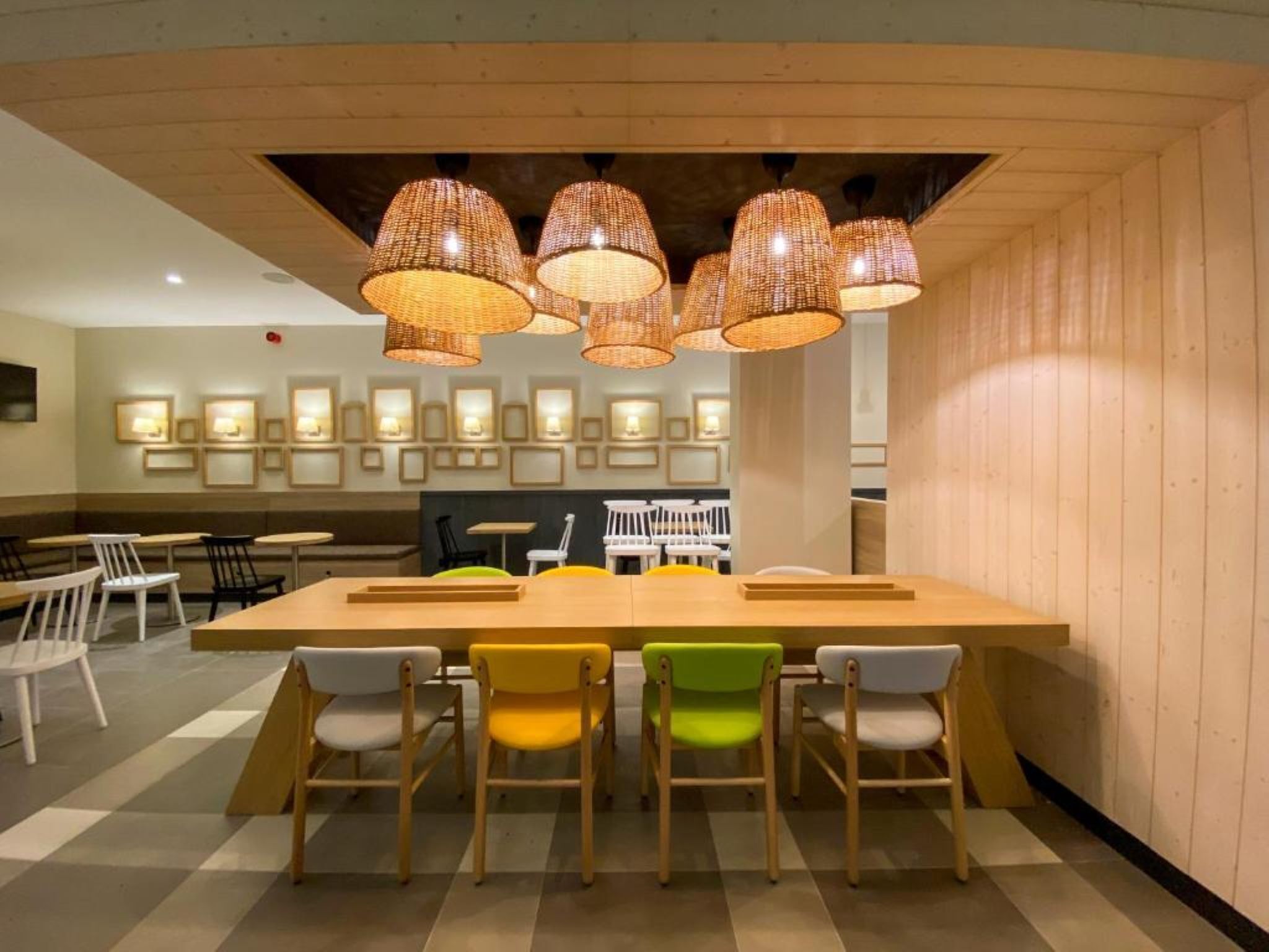 Un restaurante con una larga mesa de madera, varias sillas y lámparas de mimbre colgantes.