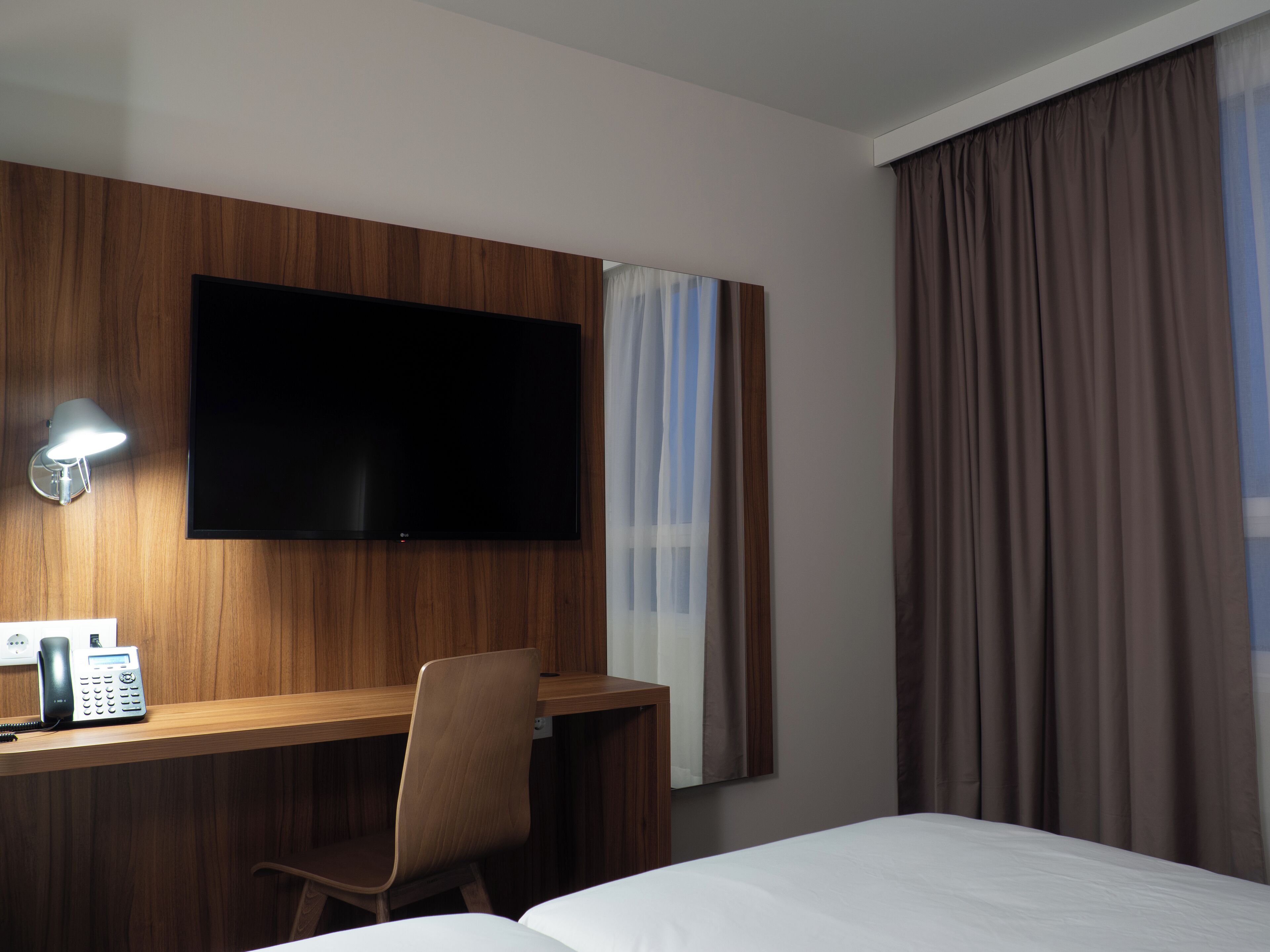 Habitación de hotel con escritorio de madera, televisor de pantalla plana, teléfono, silla y cama.
