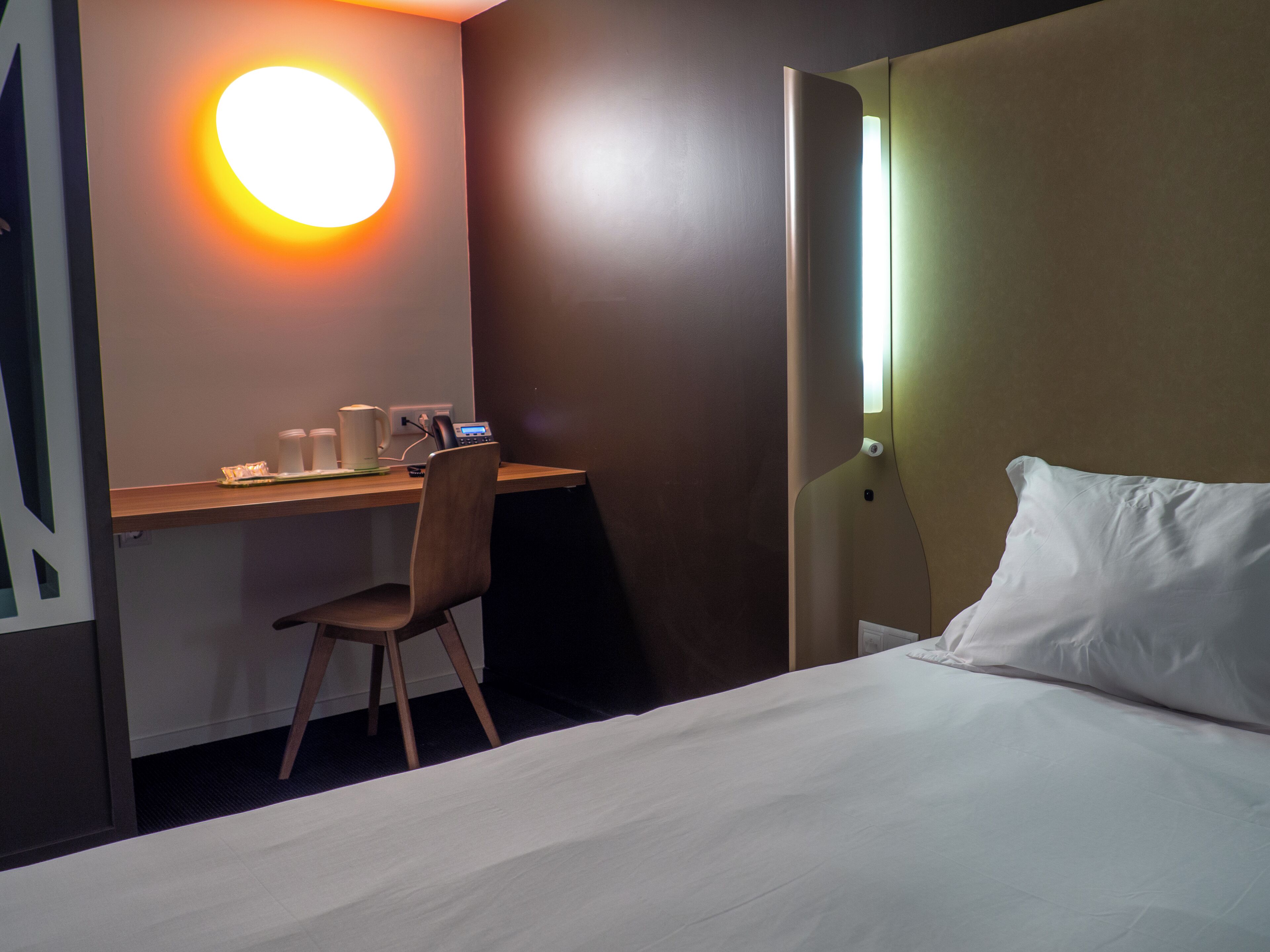 A hotel room with a bed, a desk with a chair, a coffee maker, and a phone.