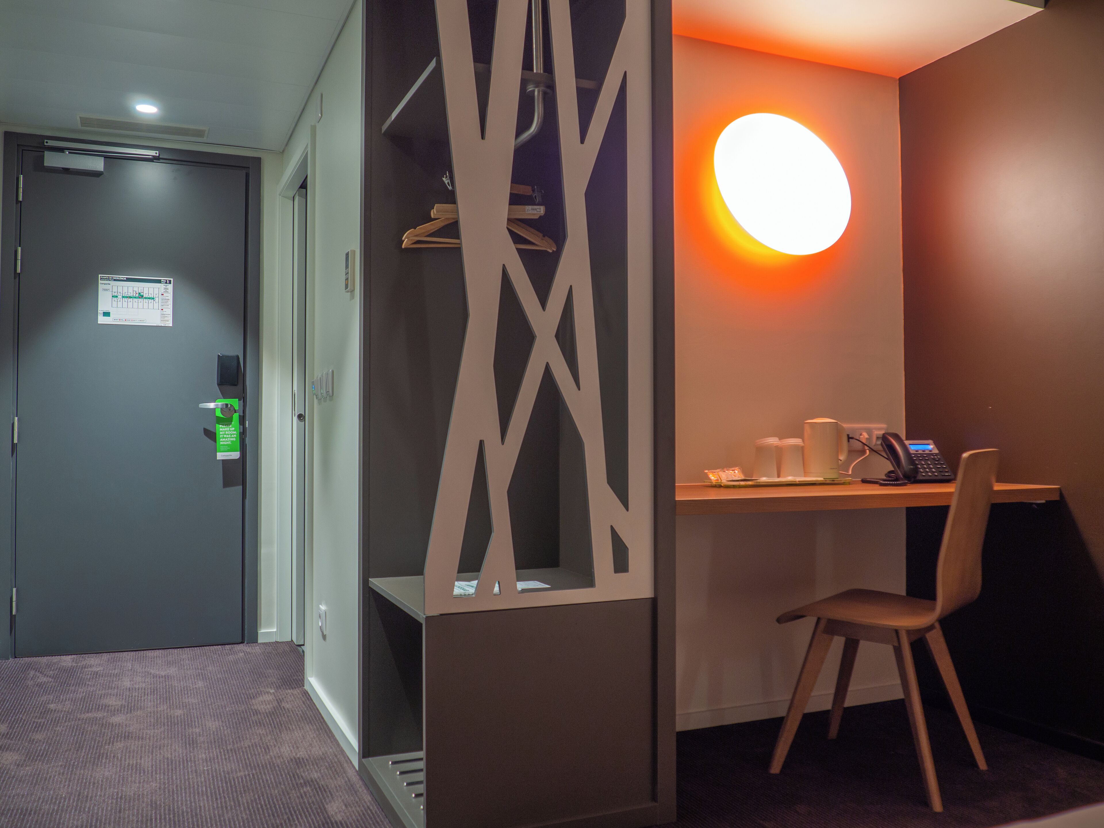 Ett hotellrum med ett skrivbord, en stol och en väggmonterad lampa.