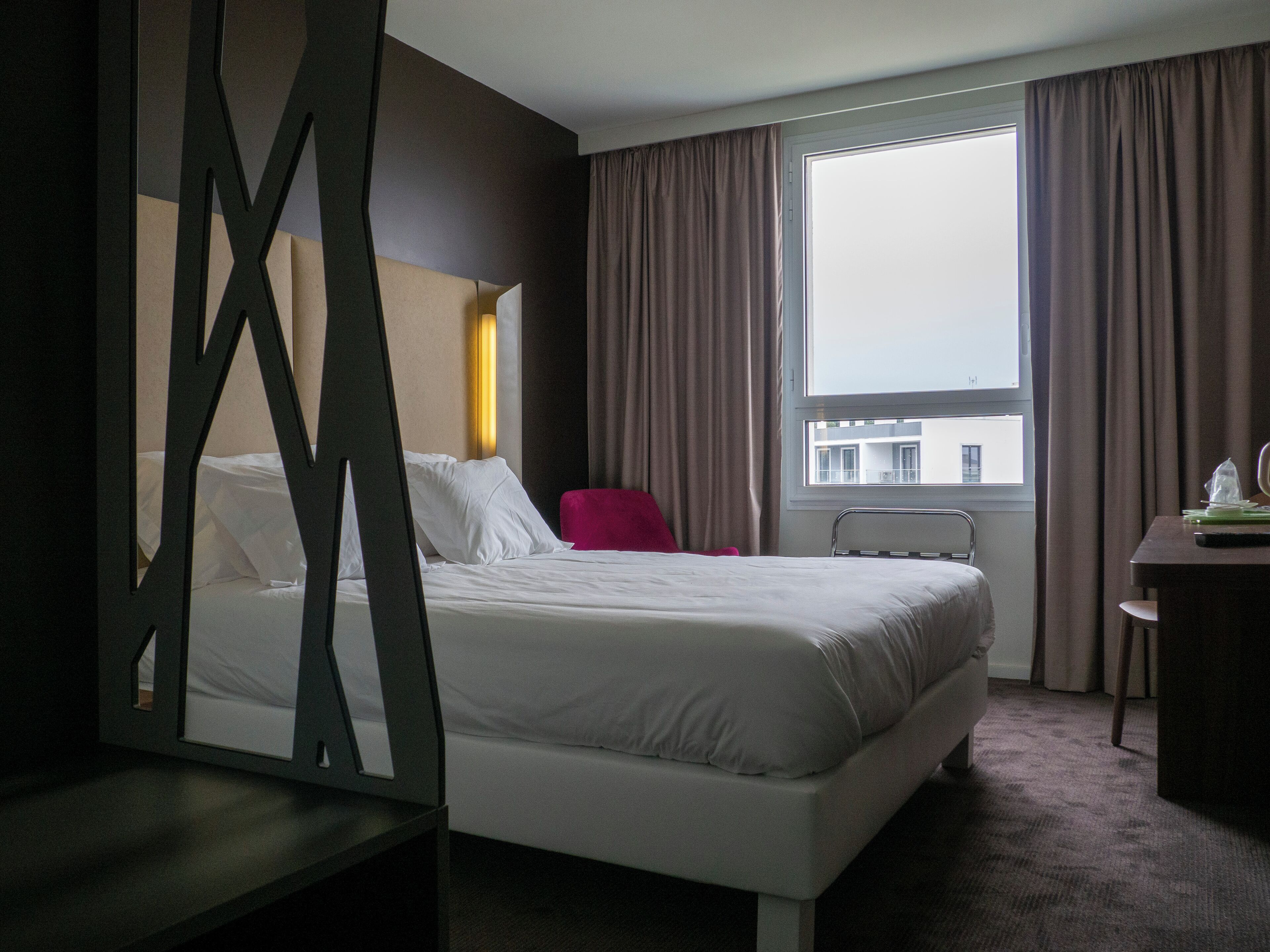 Habitación de hotel con cama, una silla, escritorio y ventana con cortinas.
