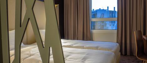 Quarto de hotel com duas camas, uma janela grande e vista para edifícios.