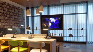 A modern living room with a wooden bookshelf, a TV, and a dining area with chairs. - Flag Hotel Caldas da Rainha (Caldas da Rainha)