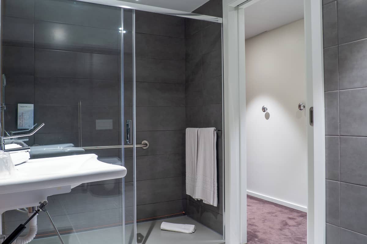A modern bathroom with a glass shower enclosure, a white sink, and a towel rack.