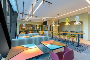 A modern restaurant interior with high tables, cushioned seating, and contemporary lighting fixtures. - Hampton by Hilton Alcobendas (Alcobendas)