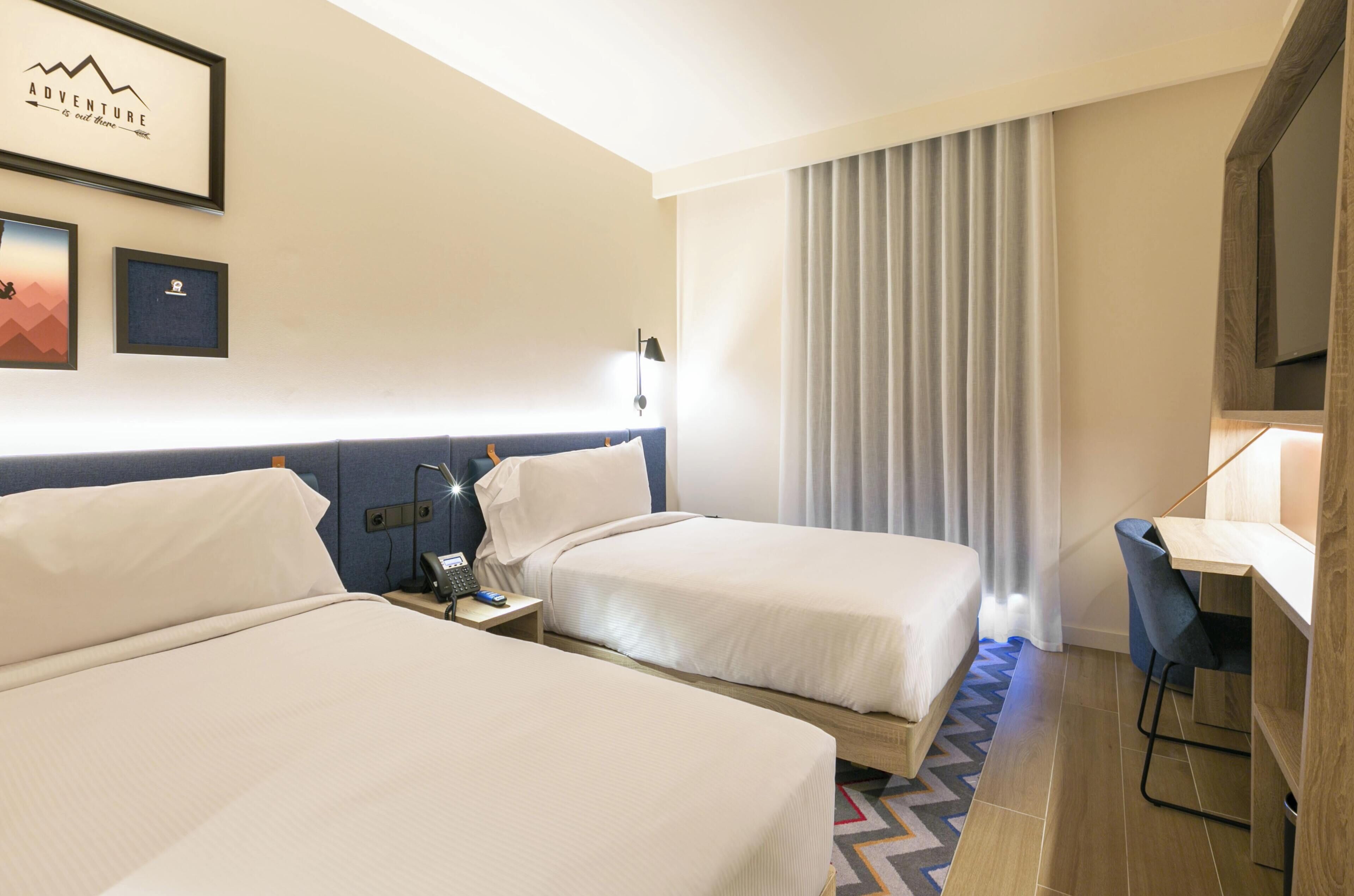A hotel room with two beds, a desk, a chair, a phone, a lamp, and a framed picture on the wall.