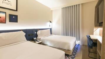 A hotel room with two beds, a desk, a chair, a phone, a lamp, and a framed picture on the wall.