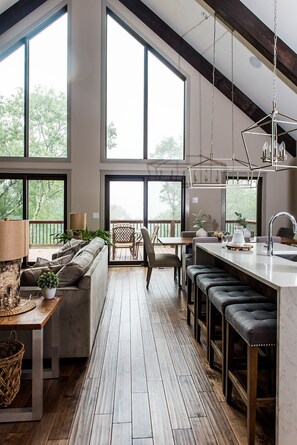 A spacious kitchen with large windows, a dining area with a wooden table and chairs, and a bar area with stools. - Designer Home: A+ Views HotTub Pool GameRoom Grill (Wintergreen Resort)