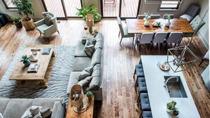 Un vaste espace de vie comprenant un canapé, une table basse et une table à manger, avec un revêtement de sol en bois et de grandes fenêtres.