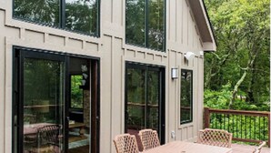 Une terrasse avec une table et des chaises, de grandes fenêtres et une vue sur les arbres.