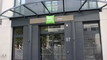 L’entrée d’un hôtel, avec un auvent en verre, une enseigne indiquant « ibis Styles Hotels » et le numéro « 97 » sur la porte.