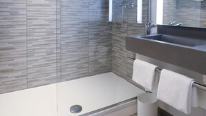 A modern bathroom with a glass-enclosed shower, a large mirror, and a vanity with a sink and towel rack. - Ibis Styles Puteaux Paris La Defense (Puteaux)