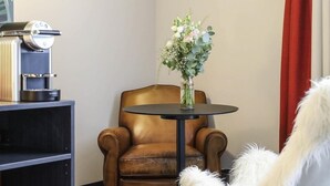 A room with a brown leather armchair, a white furry chair, a small round table, and a vase with flowers. - Ibis Styles Puteaux Paris La Defense (Puteaux)
