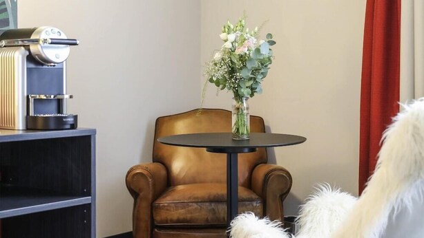 A room with a brown leather armchair, a white furry chair, a small round table, and a vase with flowers. - Ibis Styles Puteaux Paris La Defense (Puteaux)