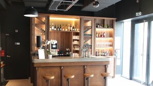 A bar area with wooden bar stools, shelves of bottles, and glasses. - Ibis Styles Puteaux Paris La Defense (Puteaux)