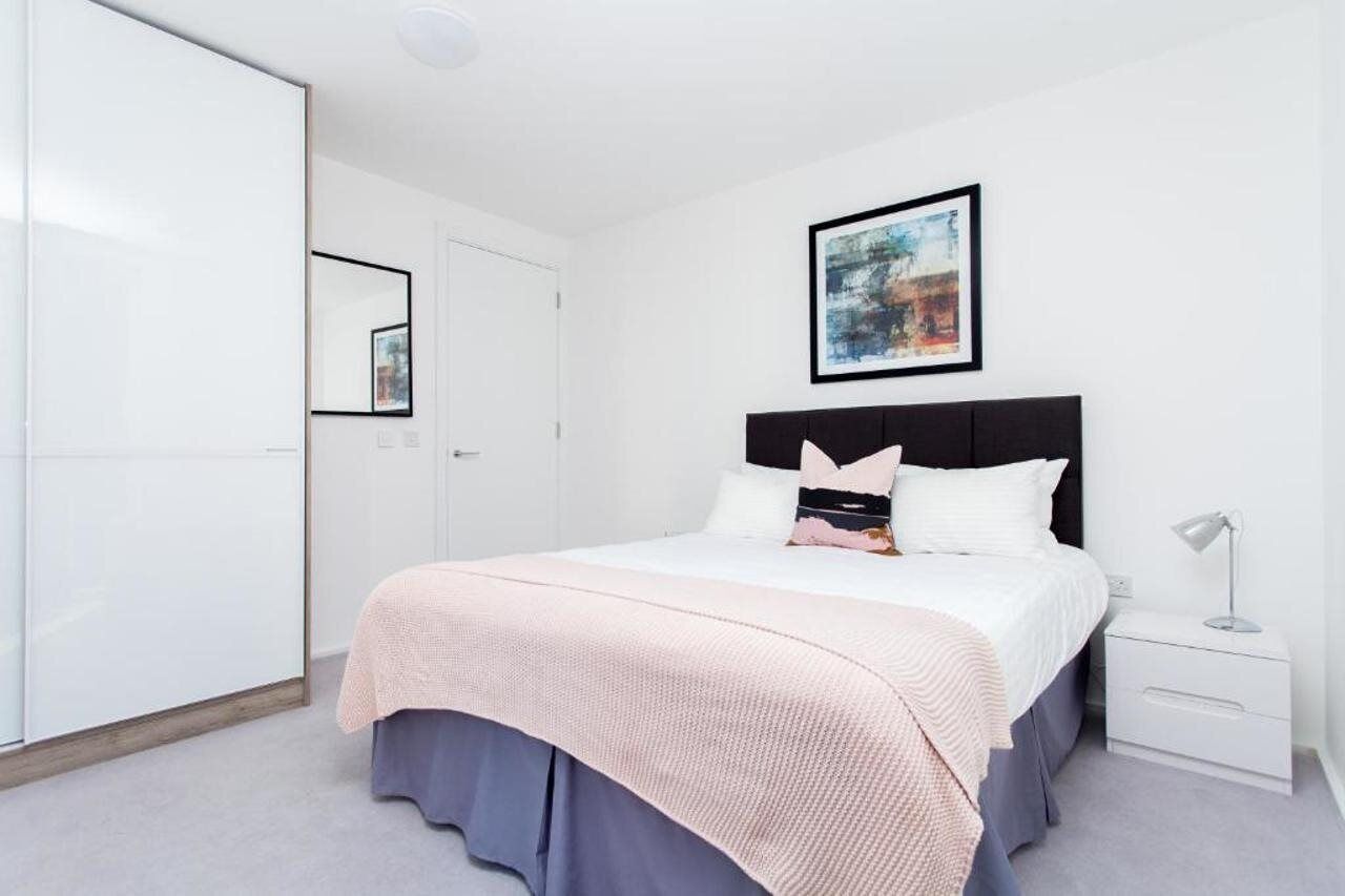 A neatly arranged bedroom with a bed, bedside table, and a framed picture on the wall.