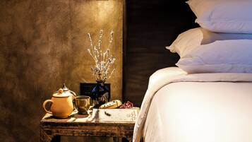 A cozy room with a bed, a nightstand with a lamp, a vase with flowers, a teapot, and slippers.
