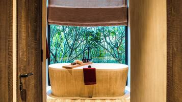 Relax in a serene bathroom with a large bathtub, wooden tray, and lush views.