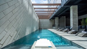 Un espace piscine intérieur moderne offrant une vue dégagée sur la piscine, des chaises longues et un banc de bronzage.