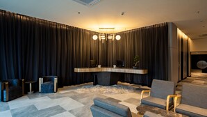 Un salon moderne avec un grand rideau foncé en arrière-plan, une table basse centrale et plusieurs options d’assises.