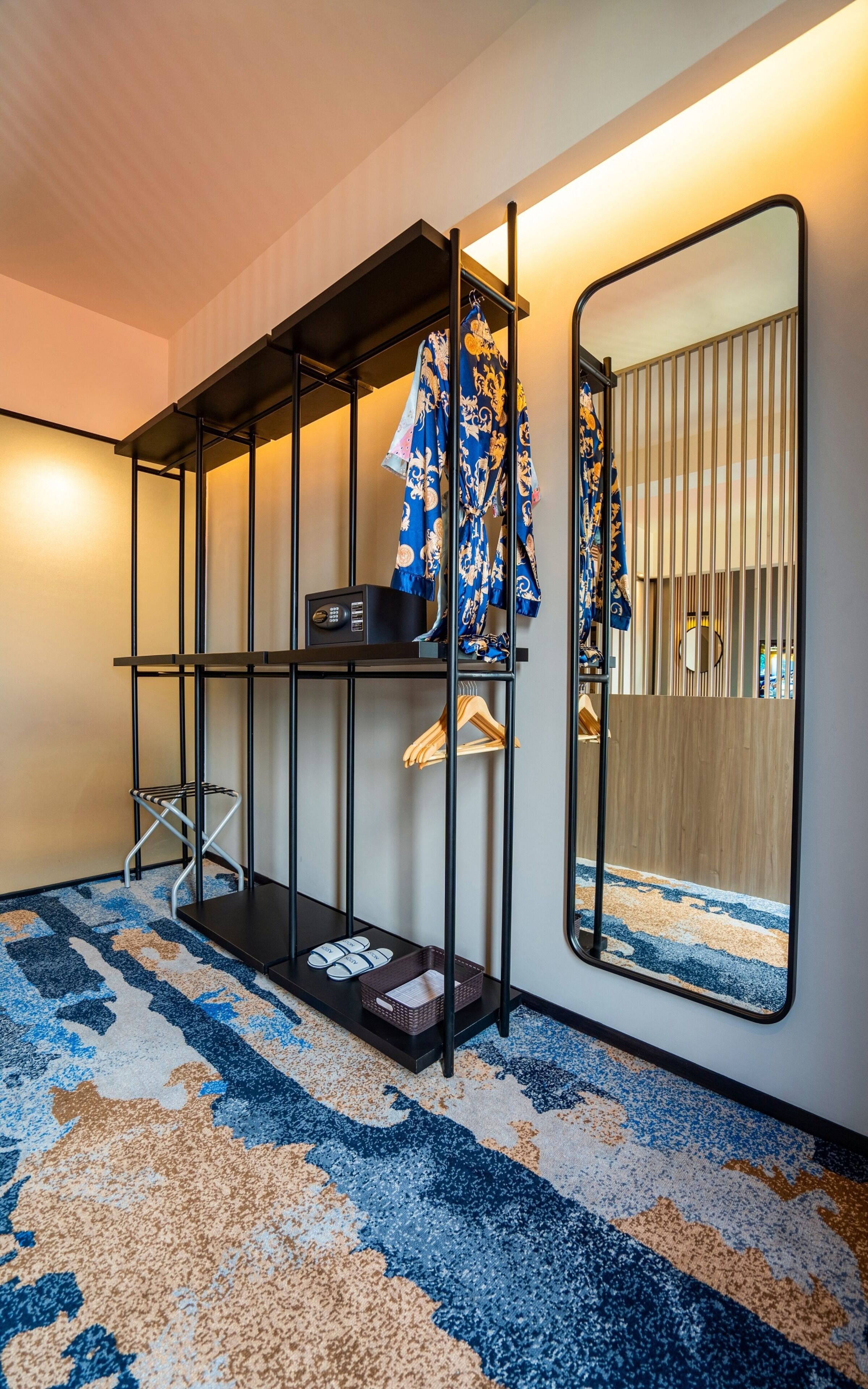 A hotel room with a black metal shelving unit, a mirror, and a patterned carpet.