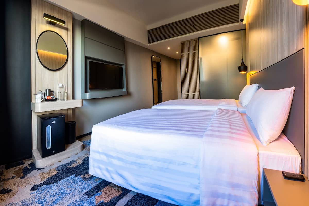 Une chambre d’hôtel avec deux lits, un téléviseur fixé au mur, un minibar et une grande fenêtre.