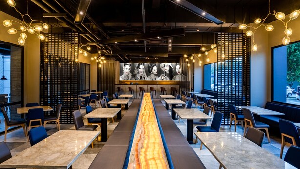 Un restaurant moderne avec une longue table centrale, des banquettes et un mur décoré de motifs.