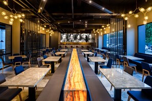 Een modern restaurant met een lange centrale tafel, zitjes en een behangetje.
