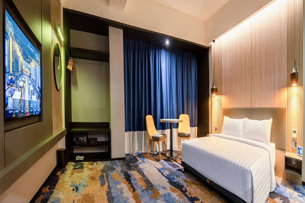 Une chambre d’hôtel comprenant un lit, un bureau avec deux chaises, une télévision et une moquette à motifs.