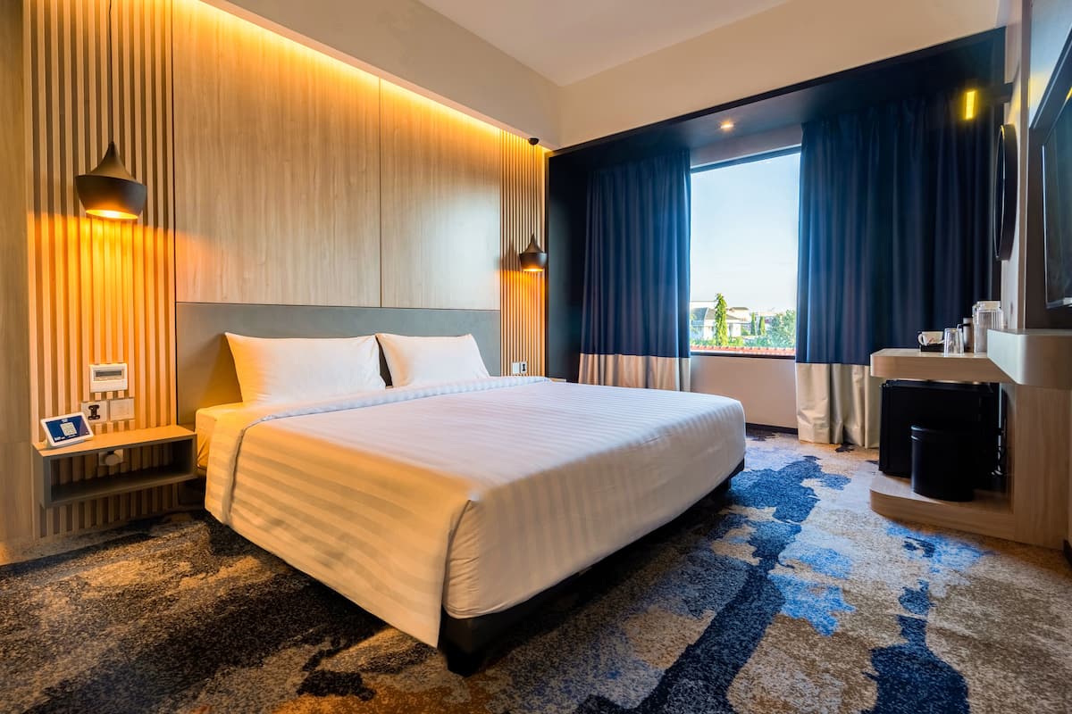 Une chambre d’hôtel avec un grand lit, un bureau équipé d’un ordinateur et une vue sur l’extérieur.