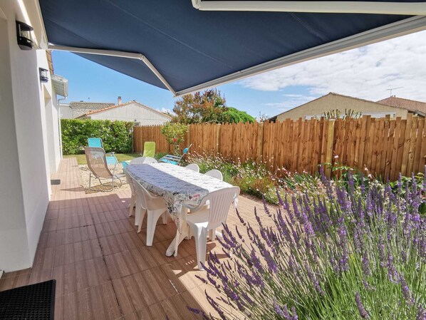 An outdoor patio with a table and chairs, a wooden fence, and lavender plants.