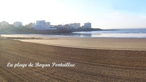 Ein Strand mit sandigem Ufer und ruhiger See. Im Hintergrund sind Gebäude zu sehen.