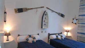 Ein Zimmer mit zwei Betten, einem Regal mit Kleinigkeiten, einem Rettungsring und einem an der Wand befestigten Regal mit einem Bootsmodell.