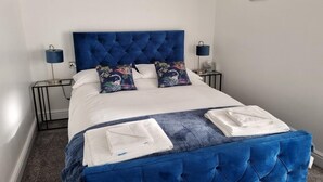 A neatly made bed with a blue headboard, white linens, and decorative pillows. - OYO The Leven (Middlesbrough)
