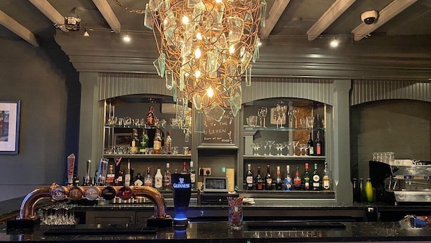 A bar area with a unique chandelier, shelves of bottles, and a counter with taps. - OYO The Leven (Middlesbrough)