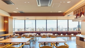 A spacious dining area with high tables and chairs, large windows with a city view, and a wooden accent wall. - Hotel Monday Premium Ueno Okachimachi (Tokyo)