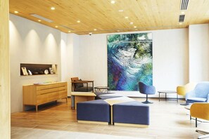 A modern interior with a wooden ceiling, a large abstract painting, a wooden cabinet, and seating arrangements. - Hotel Monday Premium Ueno Okachimachi (Tokyo)