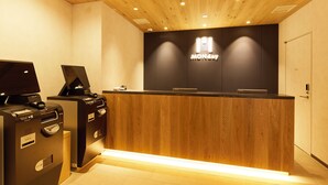 A reception desk with a wooden finish and a black countertop. There are two black ATMs on either side of the desk. - Hotel Monday Premium Ueno Okachimachi (Tokyo)