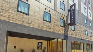 A modern hotel facade with a large entrance, potted plants, and a prominent sign for the Monday Hotel. - Hotel Monday Premium Ueno Okachimachi (Tokyo)