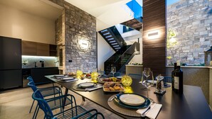 A modern dining area with a long table set for a meal, a staircase, and a stone wall. - Villa Emotha-Five Bedroom villa with Pool (Korcula)