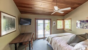 A bedroom with a wooden ceiling, a bed with pillows, a desk with a chair, a television, and a large window with blinds. - Island Property on Lake Muskoka! 4brdm, 3 bath! Best Internet! SUP, Kayak (Bracebridge)