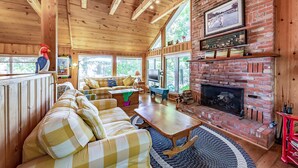 A cozy cabin interior with a checkered sofa, a fireplace, and a large window overlooking greenery. - 8 bedroom 4 bath Island getaway on Lake Rosseau! (Muskoka Lakes)