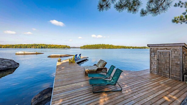 A wooden deck with lounge chairs and a small wooden structure, overlooking calm water and distant land. - 8 bedroom 4 bath Island getaway on Lake Rosseau! (Muskoka Lakes)