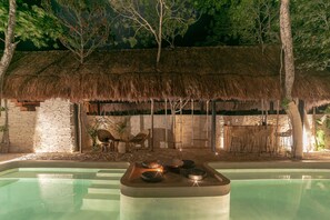 A pool area with a thatched-roof structure, stone walls, and outdoor seating. -  Zereno Tulum Beach Club Access (Tulum)