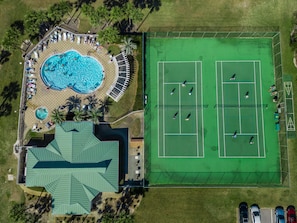 An aerial view of a resort with a swimming pool, tennis courts, and a covered area.