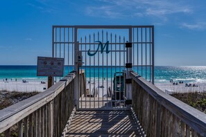A wooden boardwalk leading to a private beach with a gate marked with a large 'M'.