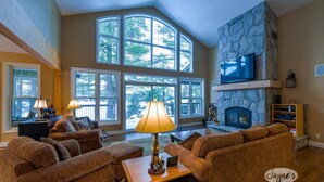 A spacious living room with large windows, a stone fireplace, and a television mounted on the wall. - 4 bedroom, 4 bath, Quiet Butterfly Lake! Port Carling! Cozy & Spacious! (Port Carling)